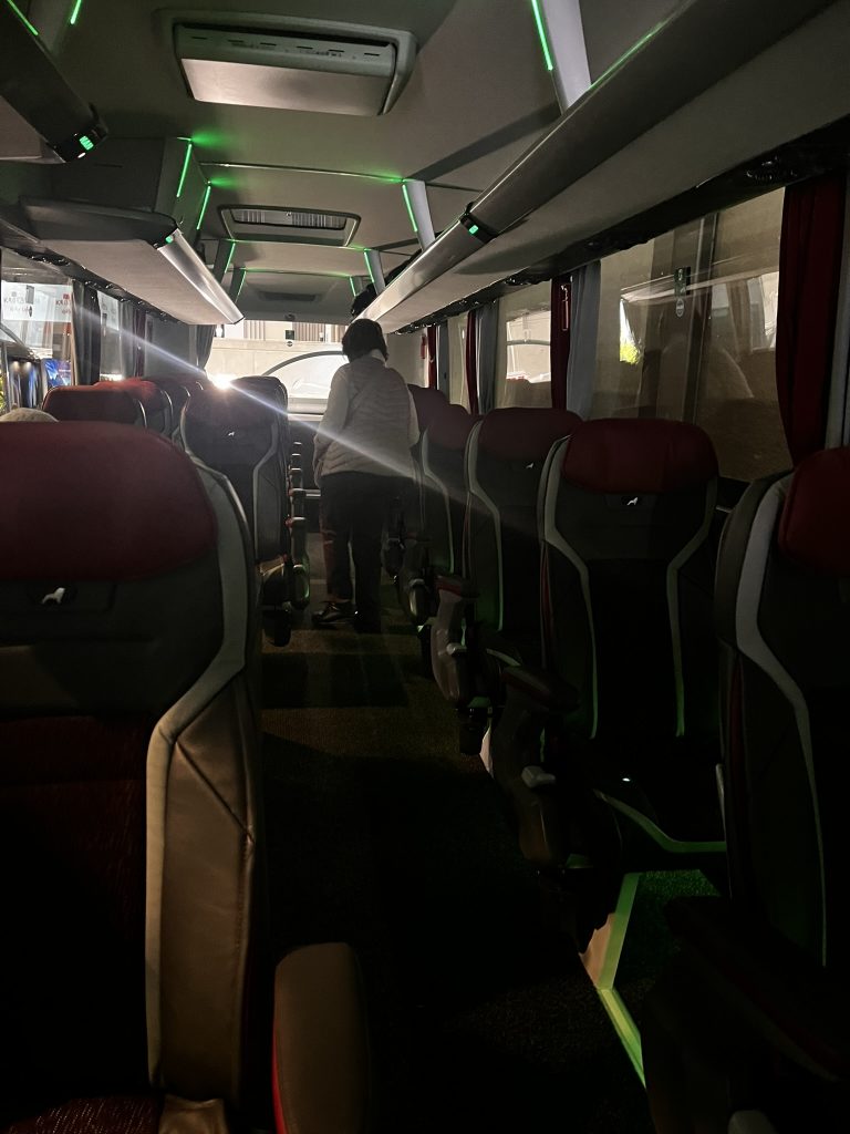 Fuchs Reisen MAN, Gang Alt-Text: Fuchs Reisen MAN Reisebus Innenansicht Gang mit roter Bestuhlung und grüner LED-Deckenbeleuchtung