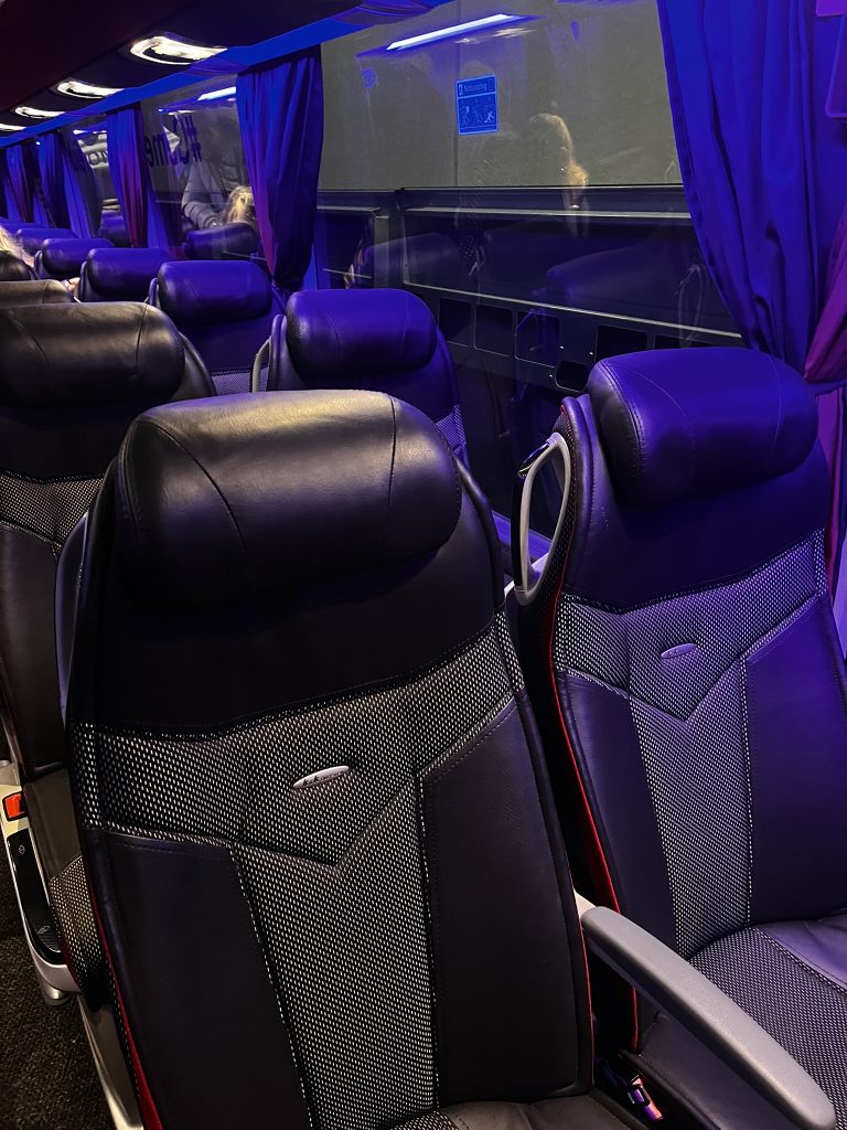 K&K Busreisen, Sitze & Fenster Alt-Text: K&K Busreisen Luxusbus breite Ledersitze mit violetter Ambientebeleuchtung und Sichttrennscheibe